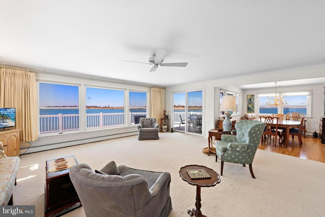 carpeted living area with a baseboard heating unit, plenty of natural light, ceiling fan with notable chandelier, and a water view