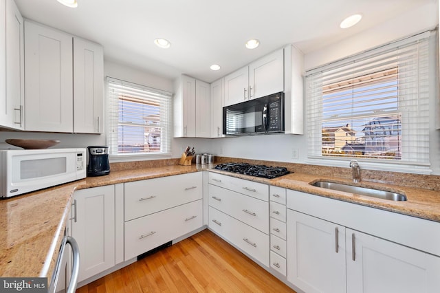 kitchen featuring light wood-type flooring, black appliances, a sink, recessed lighting, and white cabinets