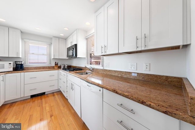 kitchen with white appliances, stone counters, a sink, white cabinetry, and light wood-type flooring