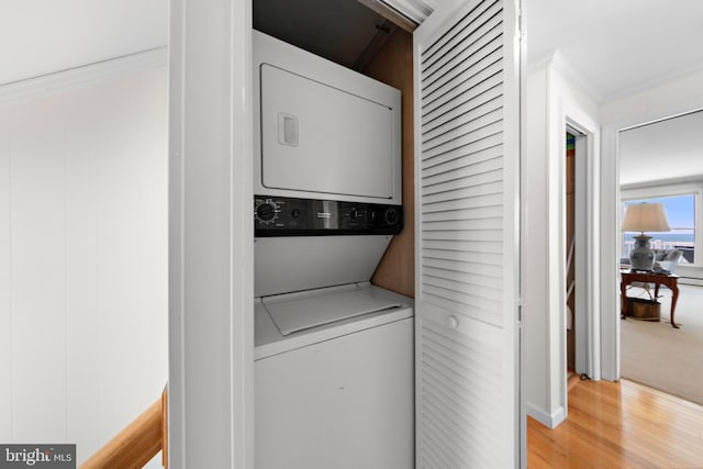 clothes washing area with laundry area, ornamental molding, wood finished floors, and stacked washing maching and dryer