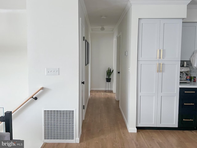 hallway with visible vents, baseboards, ornamental molding, and light wood-style flooring