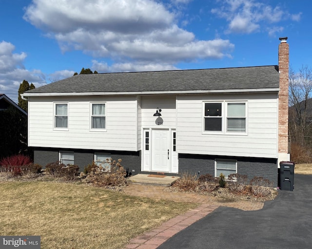 split foyer home with a front yard, roof with shingles, and a chimney