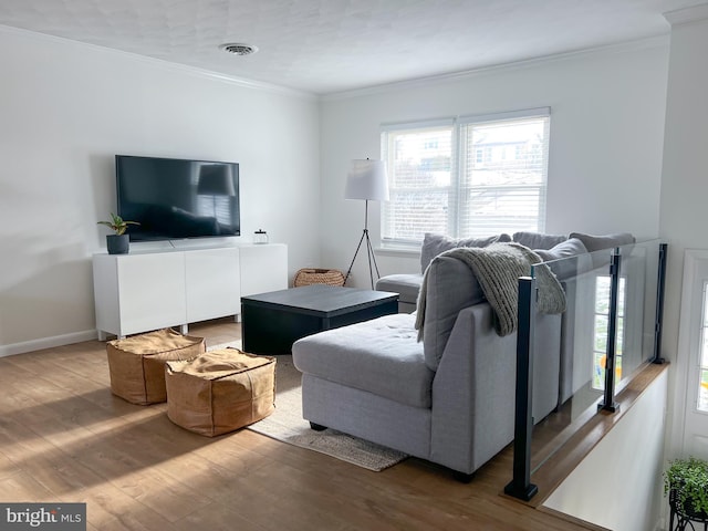 living room with crown molding, light wood-style floors, visible vents, and baseboards