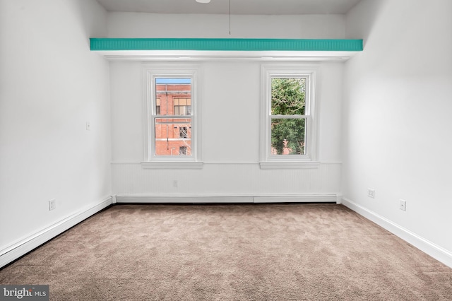 carpeted empty room with a healthy amount of sunlight, a wainscoted wall, and baseboard heating