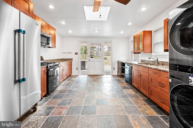 kitchen with appliances with stainless steel finishes, a skylight, brown cabinetry, and stacked washer / dryer