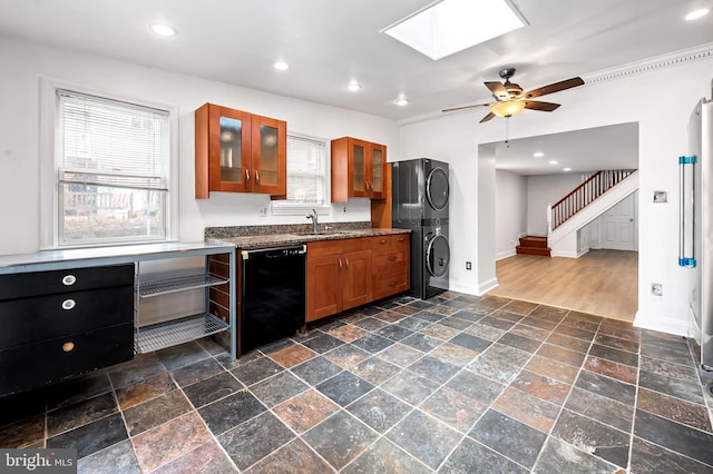 kitchen featuring black dishwasher, brown cabinets, a skylight, stacked washing maching and dryer, and stone tile flooring