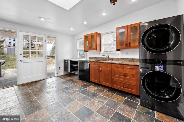 kitchen with stacked washer and dryer, a sink, stone tile flooring, brown cabinetry, and dishwasher