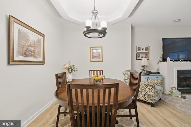 dining space featuring a fireplace, a raised ceiling, baseboards, light wood finished floors, and an inviting chandelier