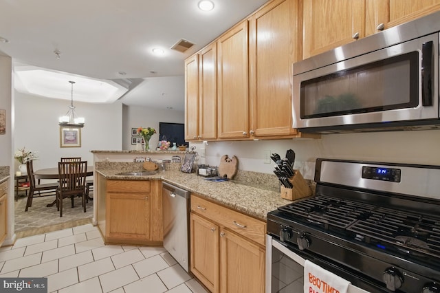 kitchen featuring appliances with stainless steel finishes, light stone counters, a sink, a peninsula, and visible vents