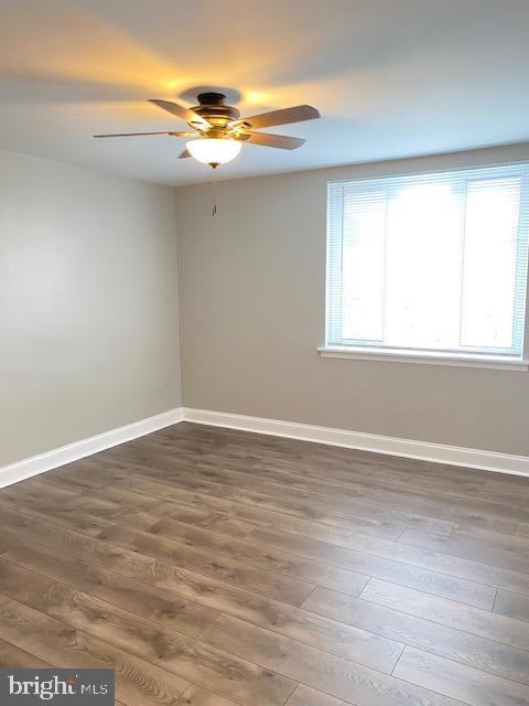 unfurnished room featuring baseboards, dark wood-type flooring, and a ceiling fan