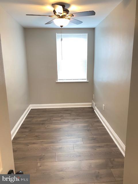 unfurnished room with dark wood-style floors, a ceiling fan, and baseboards