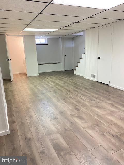 basement with stairway, a drop ceiling, visible vents, and wood finished floors