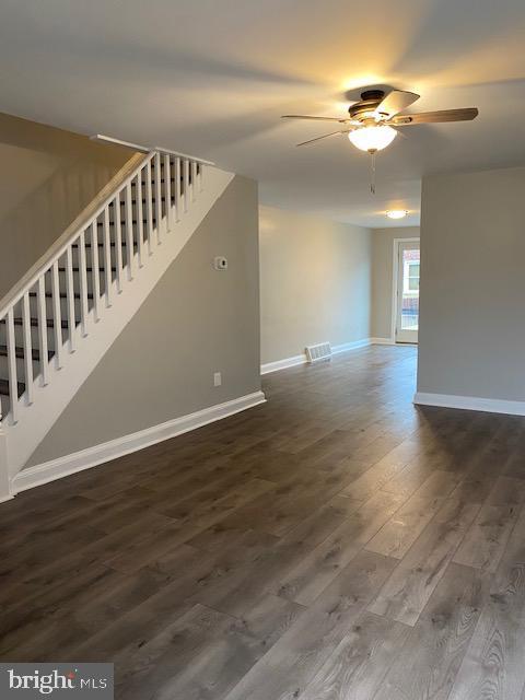 unfurnished living room with dark wood finished floors, stairway, a ceiling fan, and baseboards