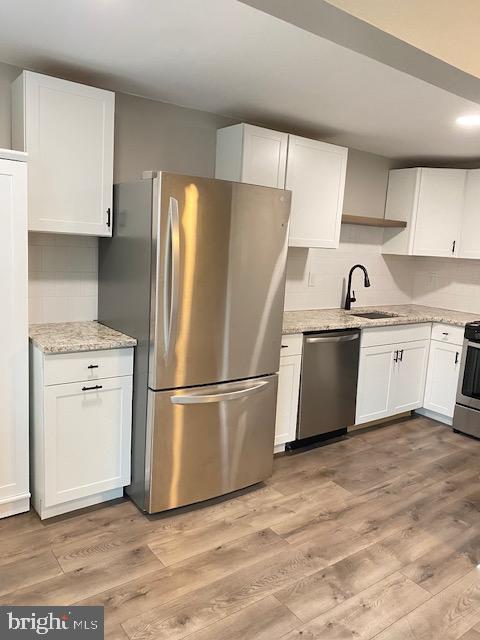 kitchen with a sink, stainless steel appliances, light wood-style floors, and white cabinets