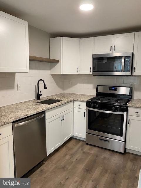 kitchen with dark wood-type flooring, a sink, light stone counters, white cabinetry, and stainless steel appliances