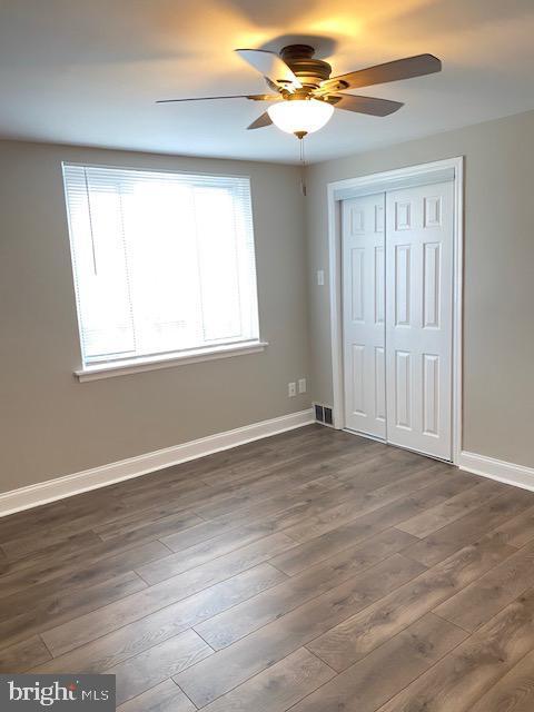 unfurnished bedroom featuring a closet, a ceiling fan, dark wood-type flooring, and baseboards