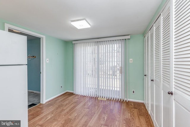 interior space with a closet, freestanding refrigerator, baseboards, and wood finished floors