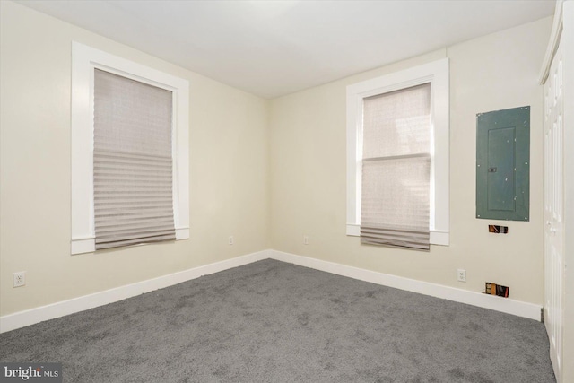 unfurnished room with electric panel, baseboards, and dark carpet