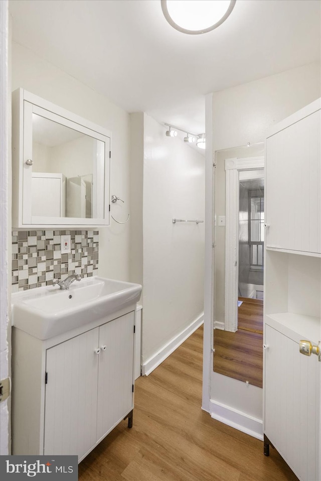 bathroom with vanity, wood finished floors, tasteful backsplash, and baseboards