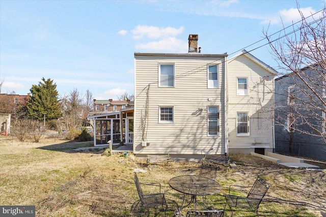 rear view of house featuring a yard, a chimney, and a sunroom