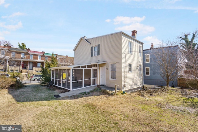 rear view of property with a lawn, a chimney, and a sunroom