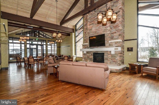 living room with beamed ceiling, a notable chandelier, high vaulted ceiling, wood-type flooring, and a fireplace