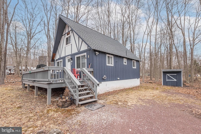 view of home's exterior featuring a deck, an outdoor structure, a storage unit, and a shingled roof