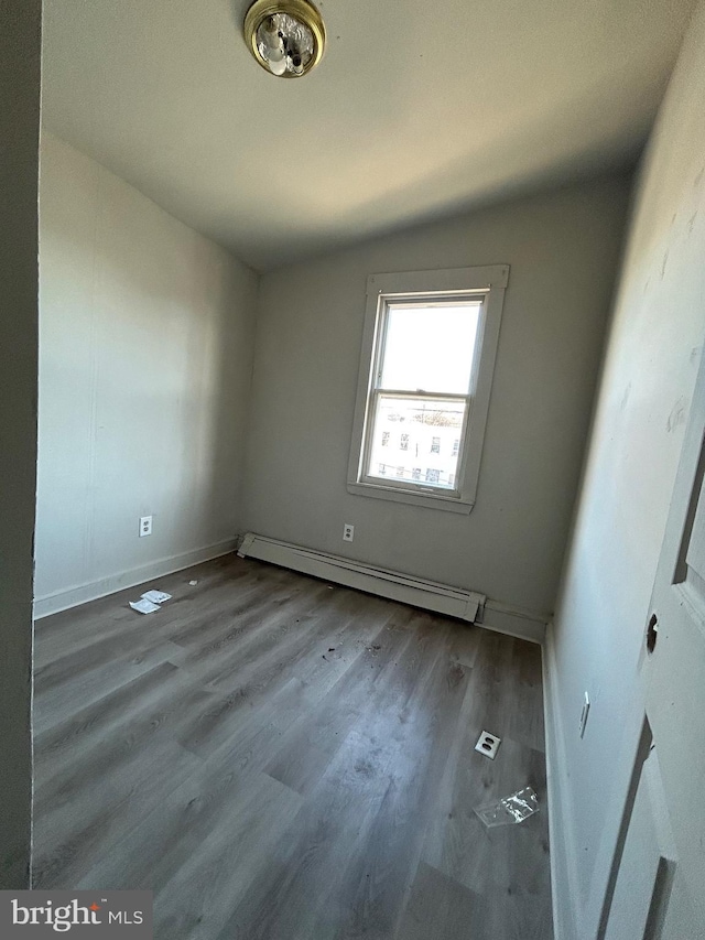 unfurnished bedroom featuring vaulted ceiling, wood finished floors, baseboards, and a baseboard radiator