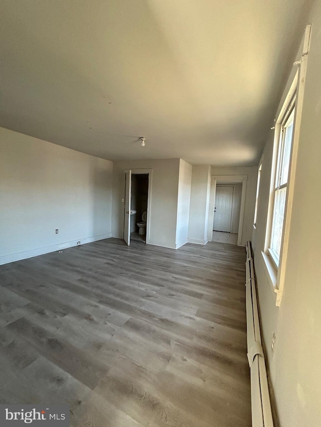 unfurnished living room featuring a baseboard heating unit and wood finished floors