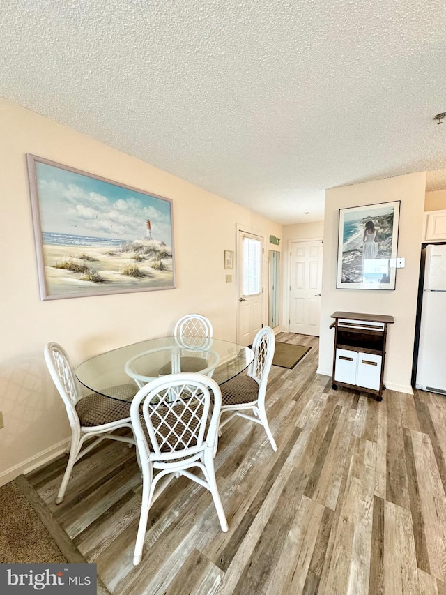 dining room featuring baseboards, a textured ceiling, and light wood-style flooring