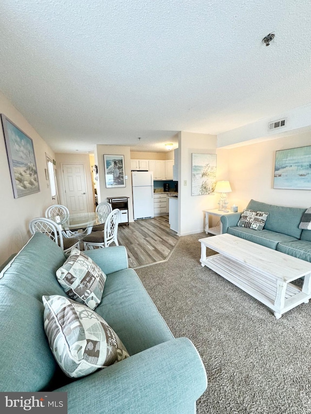 living area with light carpet, visible vents, and a textured ceiling