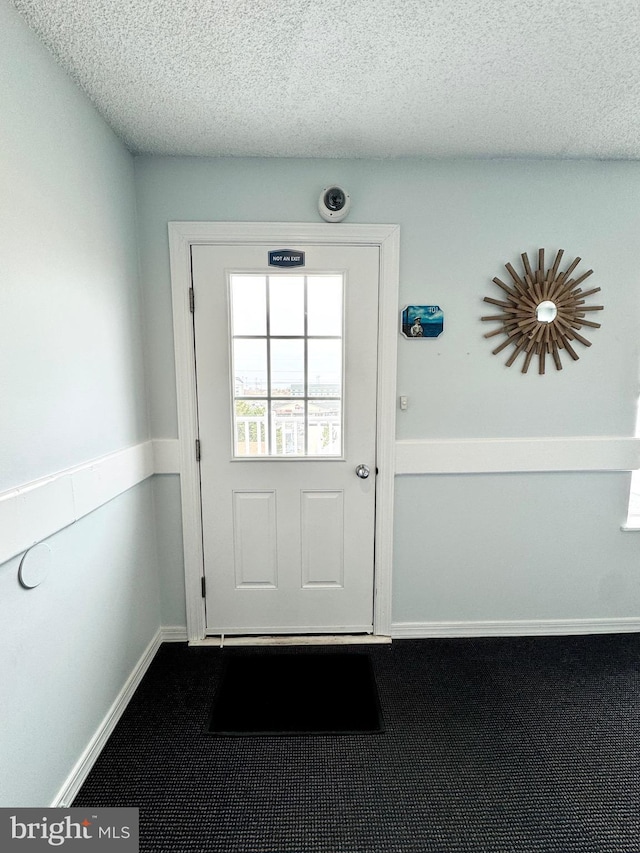 doorway to outside with baseboards, a textured ceiling, and dark carpet