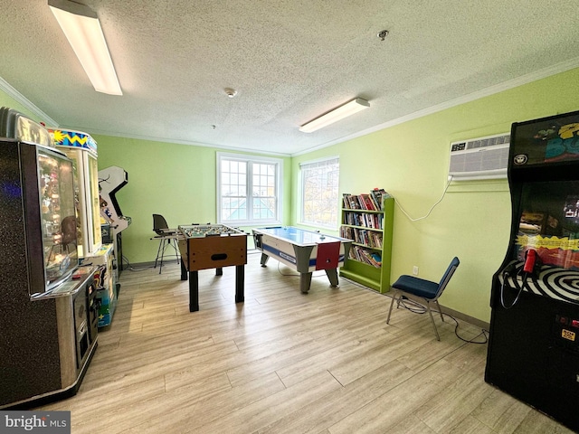 rec room with a wall mounted air conditioner, a textured ceiling, crown molding, light wood finished floors, and baseboards