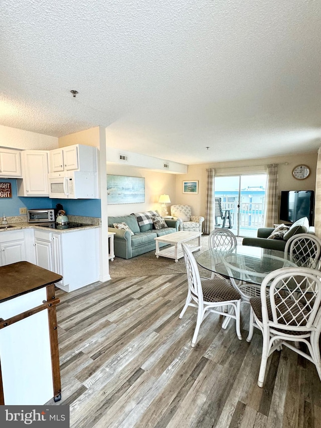 dining space featuring visible vents, a textured ceiling, wood finished floors, and a toaster