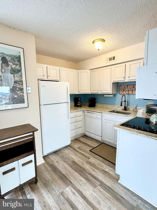 kitchen featuring white appliances, visible vents, light wood finished floors, a sink, and white cabinetry