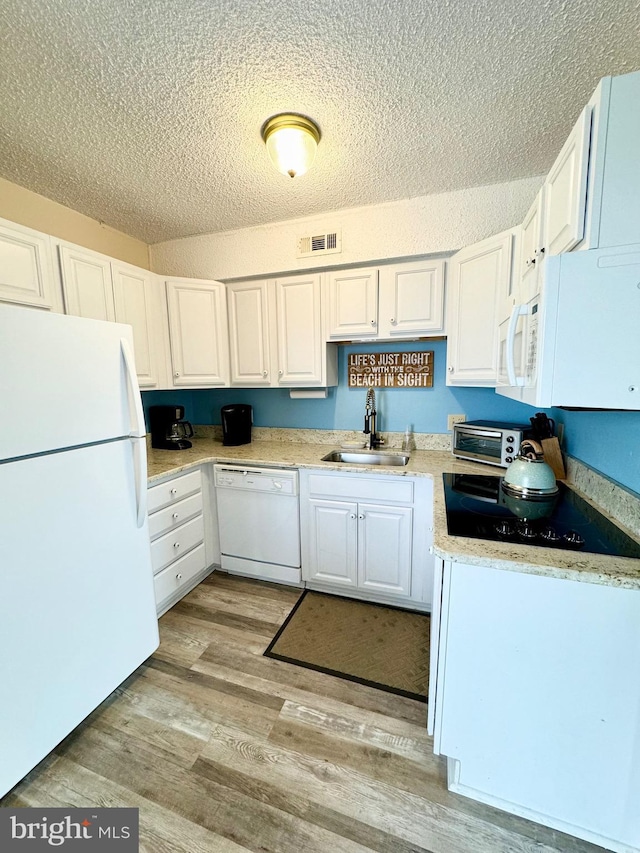 kitchen with visible vents, light wood-type flooring, white cabinets, white appliances, and a sink