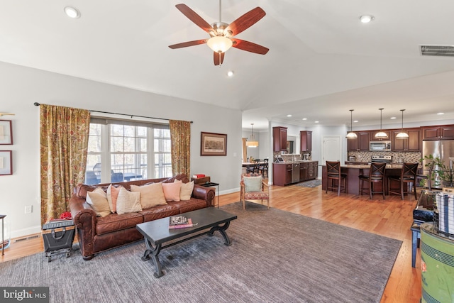 living area with vaulted ceiling, visible vents, light wood finished floors, and ceiling fan