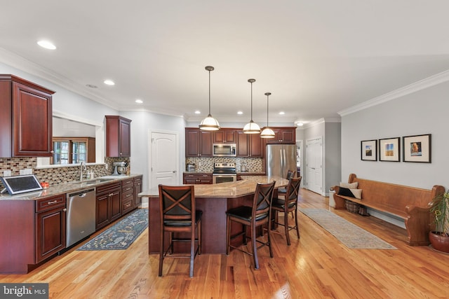 kitchen with a breakfast bar, light wood finished floors, stainless steel appliances, and ornamental molding