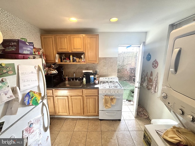 kitchen featuring a sink, dark countertops, white appliances, light tile patterned flooring, and stacked washer / dryer