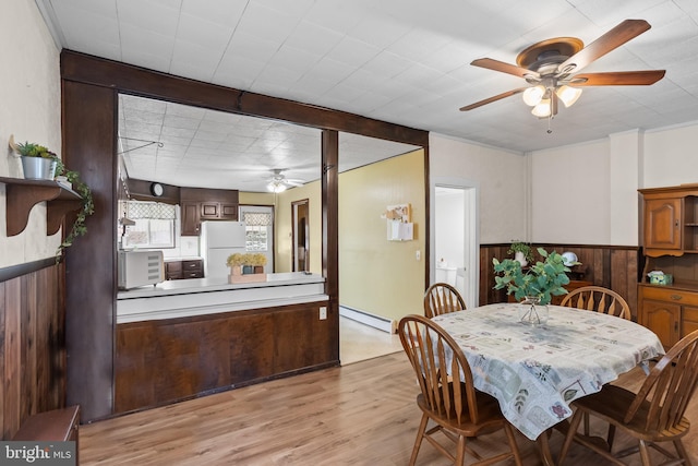 dining area featuring ceiling fan, a wainscoted wall, wood walls, light wood-style flooring, and a baseboard radiator