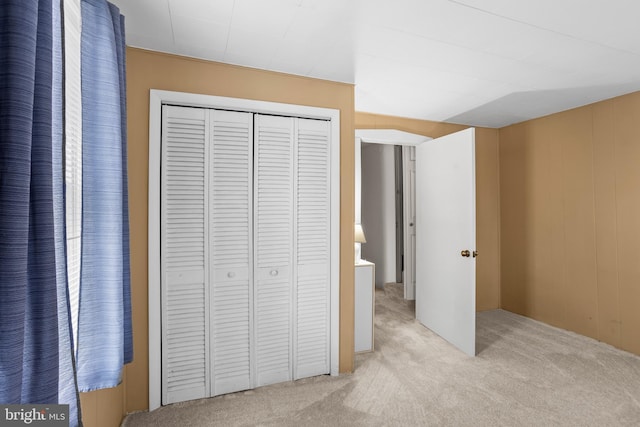 unfurnished bedroom featuring a closet, light carpet, and wooden walls