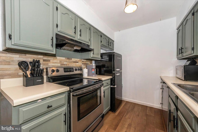 kitchen with light countertops, stainless steel appliances, decorative backsplash, under cabinet range hood, and dark wood-style floors