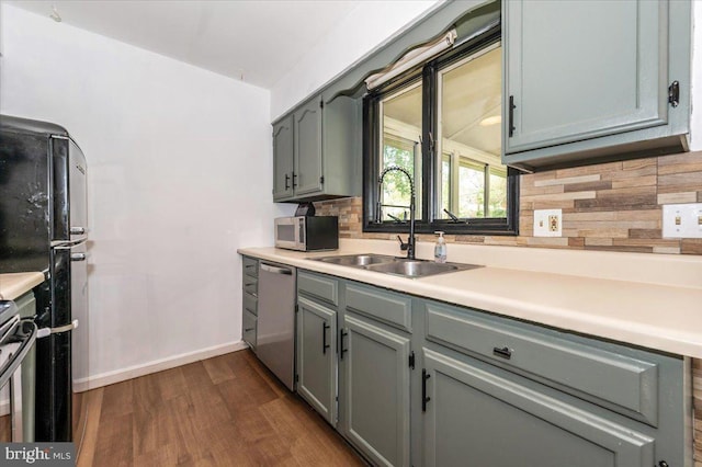 kitchen with dark wood-type flooring, gray cabinets, a sink, backsplash, and stainless steel appliances