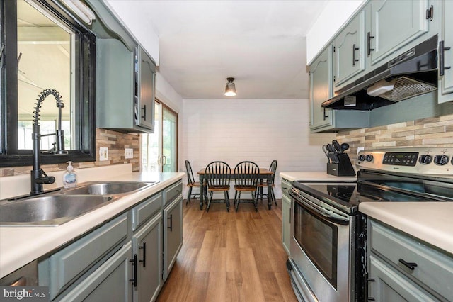 kitchen featuring backsplash, wood finished floors, stainless steel range with electric cooktop, a sink, and under cabinet range hood