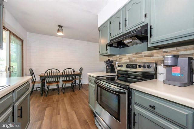 kitchen featuring light countertops, backsplash, under cabinet range hood, and stainless steel range with electric stovetop