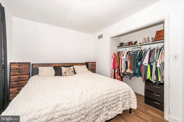 bedroom with baseboards, visible vents, wood finished floors, and a closet