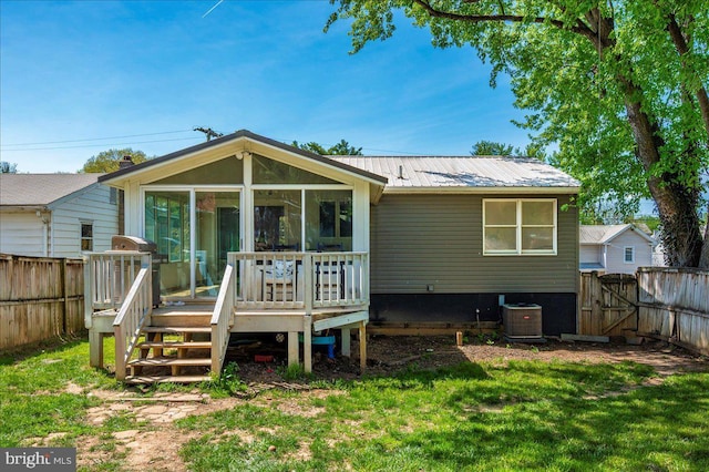 rear view of property featuring a deck, a fenced backyard, a sunroom, metal roof, and a yard
