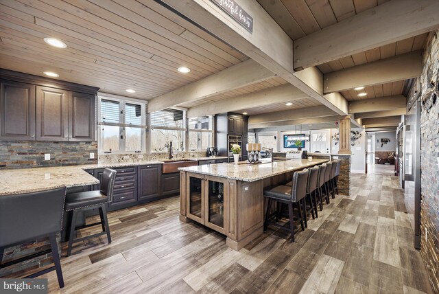 kitchen with light stone counters, beam ceiling, light wood-style flooring, and a breakfast bar area