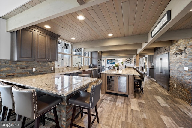 kitchen with a peninsula, a sink, built in refrigerator, wooden ceiling, and a kitchen breakfast bar