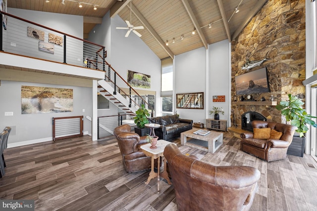 living area featuring a stone fireplace, wooden ceiling, track lighting, and wood finished floors